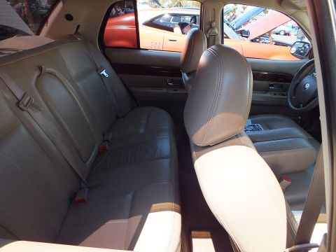 2003 Ford Crown Victoria - Interior of a full-size sedan showing the tan leather rear bench seat and front seatbacks with a Ford emblem on the dash.