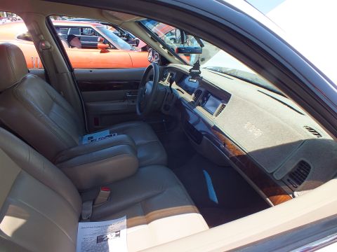 2003 Ford Crown Victoria - Front cabin of a sedan showing the dark dashboard, steering wheel, and tan leather front seats with a printed info sheet.