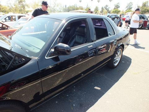 2003 Ford Crown Victoria - Side profile of a glossy black four-door full-size sedan with silver wheels, parked among cars and spectators at a show.