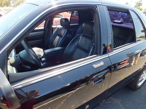 2003 Ford Crown Victoria - View through the side windows of a black sedan revealing black leather seats and chrome trim around the doors.