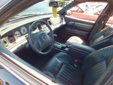2003 Ford Crown Victoria - Front interior of a sedan with black leather seats and a steering wheel bearing a Mercury emblem, parked outdoors.