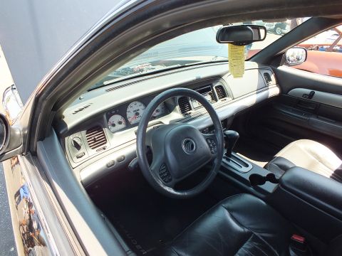 2003 Ford Crown Victoria - Front cabin of a sedan showing a Mercury-emblem steering wheel, gauge cluster, and black leather seats.