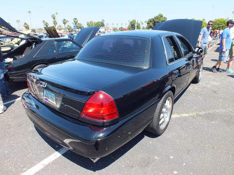 2003 Ford Crown Victoria - Rear three-quarter view of a black Mercury four-door sedan with red taillights, parked at a crowded car show.