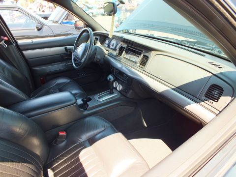 2003 Ford Crown Victoria - Front cabin of a sedan with a Mercury-emblem steering wheel, woodgrain trim, and black and tan leather seats.