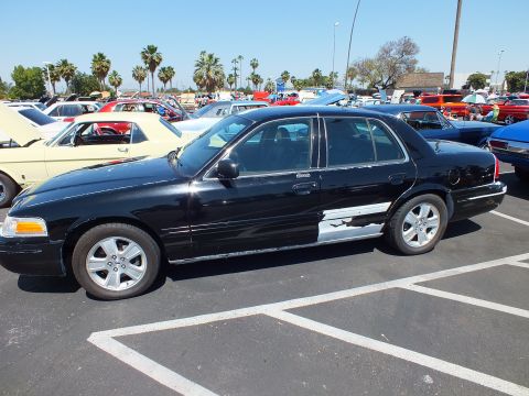 2003 Ford Crown Victoria - Side profile of a black four-door full-size sedan with silver wheels, parked among many cars at an outdoor show.