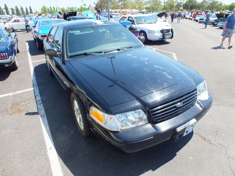 2003 Ford Crown Victoria - Front three-quarter view of a black Ford four-door sedan with the oval grille badge, parked among show cars.