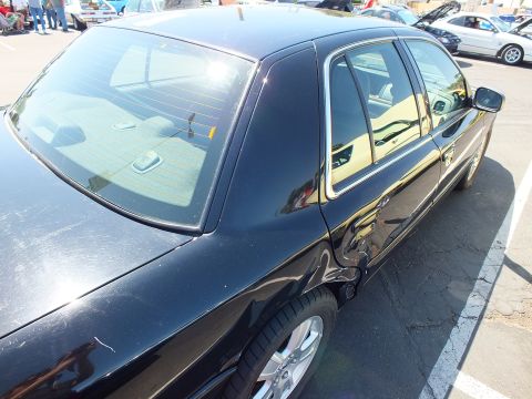 2003 Ford Crown Victoria - Rear three-quarter view of a black four-door sedan showing the rear window, tan interior, and silver wheel.