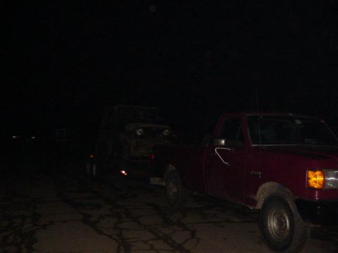 1992 Ford Bronco - A red pickup truck tows a trailer carrying another vehicle in the dark.