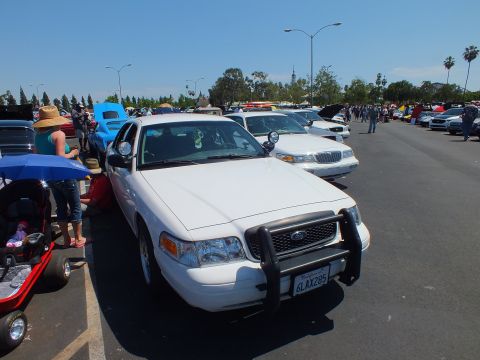 2003 Ford Crown Victoria - White Ford full-size sedan with a black push bar and plate 6LAX285, parked in a row of cars at an outdoor show.