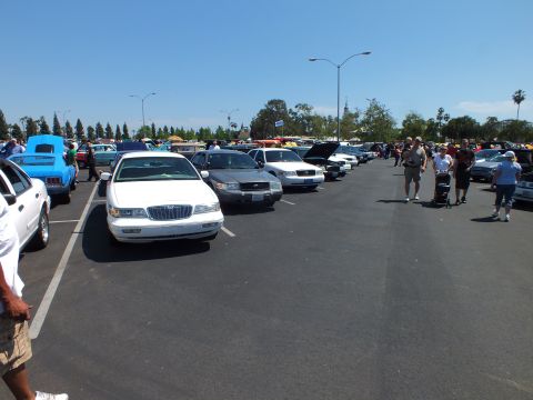 2003 Ford Crown Victoria - white Mercury sedan parked at the head of a row of cars while attendees stroll the lanes of an outdoor car show.