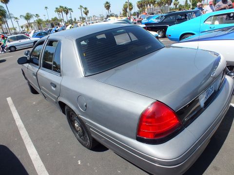 2003 Ford Crown Victoria - rear three-quarter view of a silver Ford sedan parked at an outdoor car show with palm trees in the background.