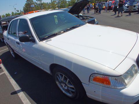 2003 Ford Crown Victoria - white Ford sedan with its hood raised and five-spoke aftermarket wheels displayed at a car show.