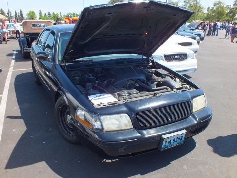2003 Ford Crown Victoria - black Ford sedan with its hood open revealing the engine bay, displayed at an outdoor car show.