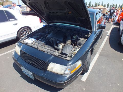2003 Ford Crown Victoria - dark teal Ford sedan with its hood raised showing the engine bay, parked at a car show with a Nevada-style plate.
