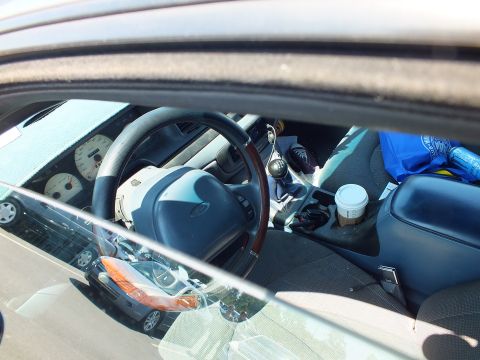 2003 Ford Crown Victoria - interior of a sedan seen through the open door window, showing a wood-rimmed steering wheel, gauges and a coffee cup.