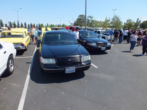 2003 Ford Crown Victoria - black Ford sedan with California plate 6LQH600 parked at a crowded outdoor car show.