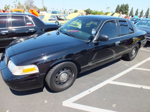2003 Ford Crown Victoria - black Ford sedan with black steel wheels parked in a marked stall at a sunny outdoor car meet.