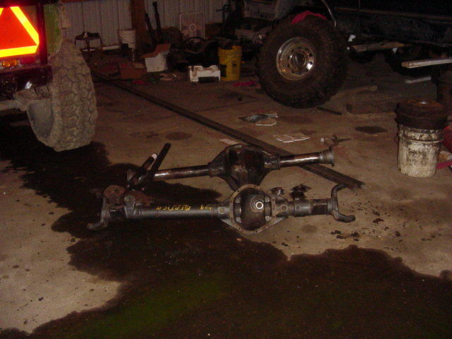Two Ford Bronco rear axles on a garage floor. One axle has "1991 Bronco" written on it