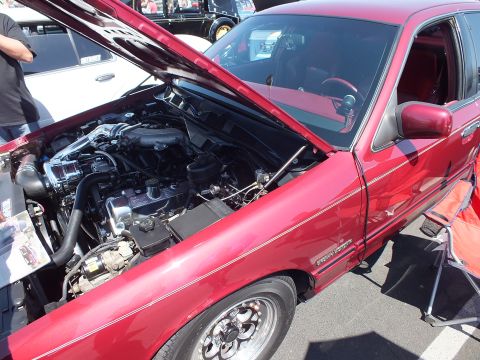 2003 Ford Crown Victoria - Front quarter of a red sedan with its hood up revealing the engine and a matching red interior at an outdoor car show.