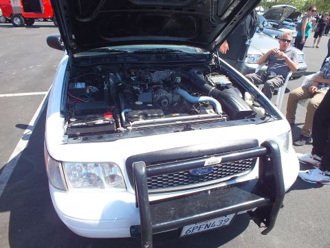 2003 Ford Crown Victoria - white Ford SUV with its hood open and a black brush guard, showing the engine bay, parked in a lot with spectators seated nearby.