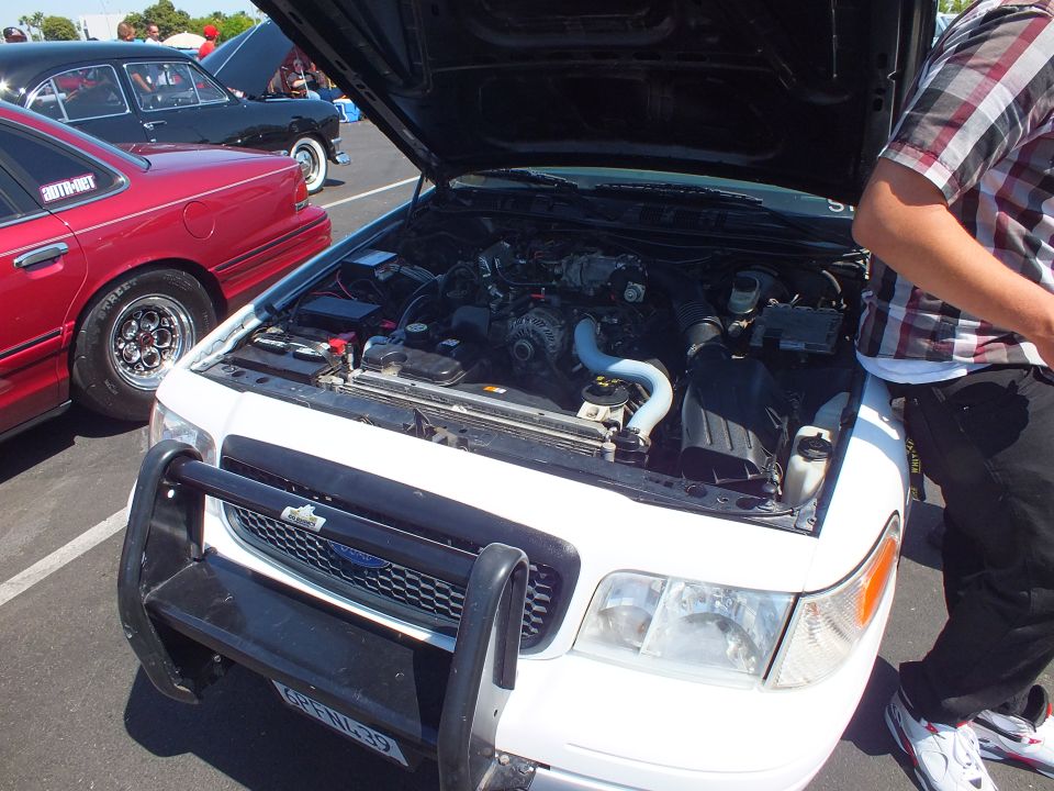 White SUV with open hood and brush guard showing engine, red sedan in background at car show
