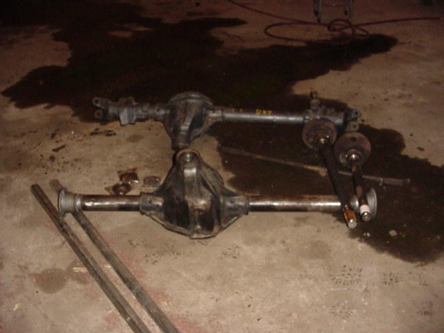 Two vehicle rear axles are on the floor. One is above the other