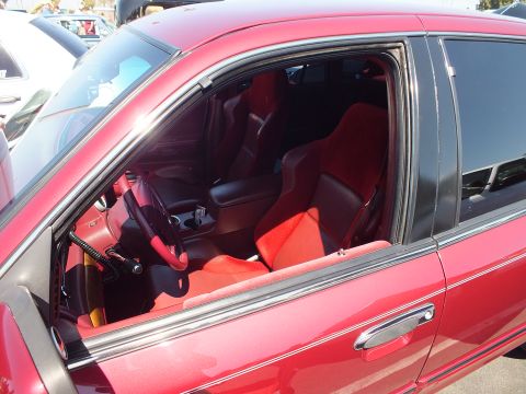 2003 Ford Crown Victoria - View through the open window of a red car showing custom red-and-black sport bucket seats and a leather-wrapped steering wheel.