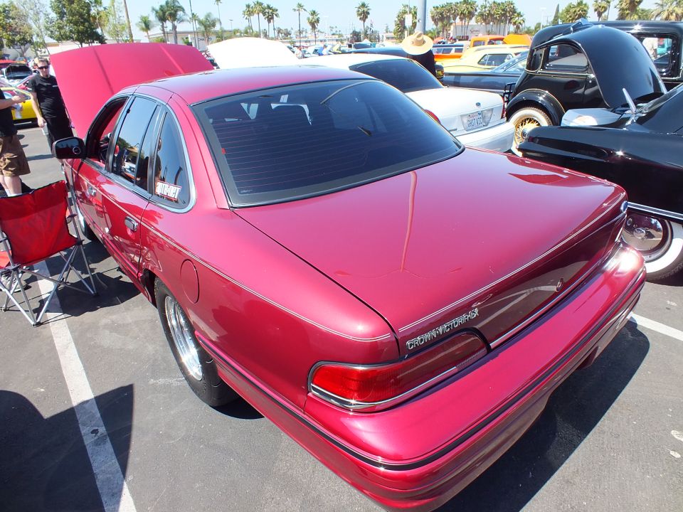 Rear three-quarter of a metallic red Ford sedan with open hood and drag wheels at a car show