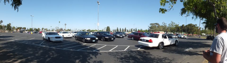 Panoramic view of a sunny parking lot with sedans including a white police-style car
