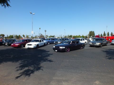 Lowered purple sedan with pink wheels among parked cars in a sunny lot