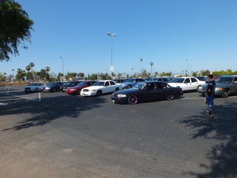 Lowered black sedan on pink wheels and a person in a sunny parking lot