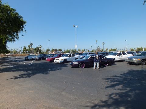 Person beside a lowered dark sedan wearing a number-17 jersey in a sunny lot