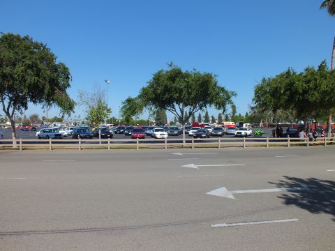 Cars lined up in a parking lot behind a low wooden fence on a sunny day