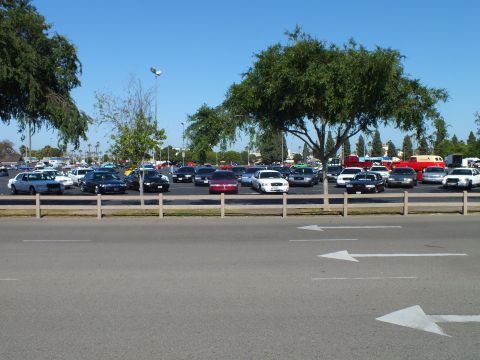 Full-size sedans parked in a lot behind a low wooden rail fence