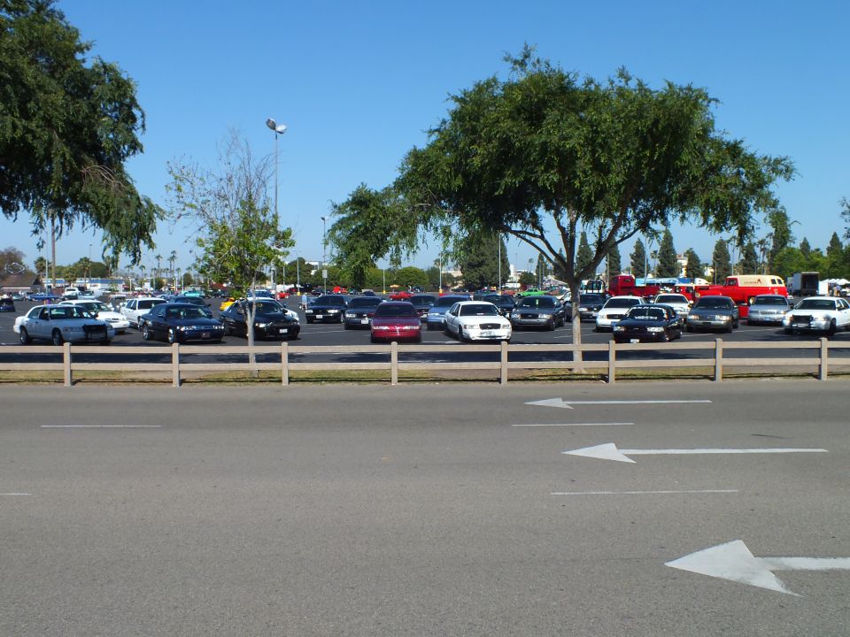 Full-size sedans parked in a lot behind a low wooden rail fence