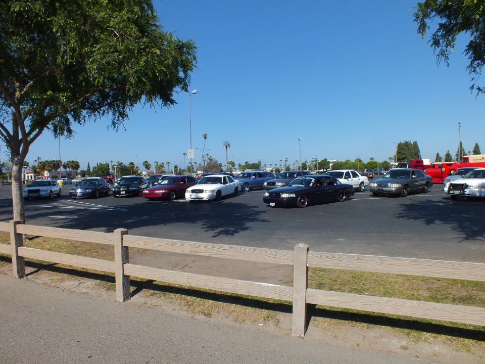 Cars including a lowered black sedan parked across a sunny lot