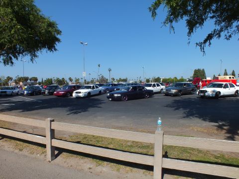 Lowered dark sedan among parked cars in a wide sunny lot