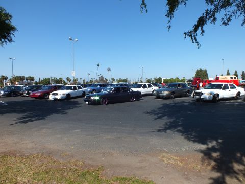Lowered dark sedan driving across a parking lot among parked cars
