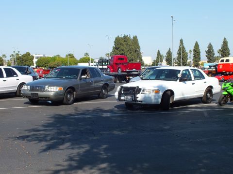 Silver and white Ford Crown Victoria sedans parked in a sunny lot with a red flatbed truck behind