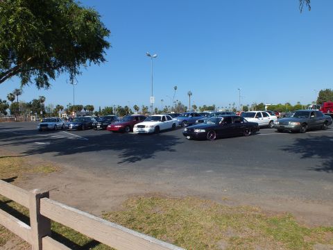 Group of sedans parked in a large lot behind a wooden rail fence under blue sky