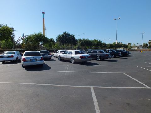 Row of sedans in a lot with a tall striped amusement park drop tower in the distance