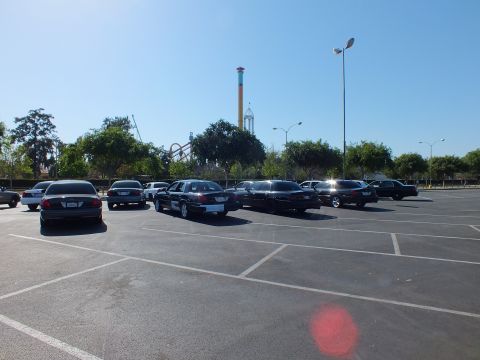 Dark sedans angled in a parking lot with a tall striped drop tower behind trees