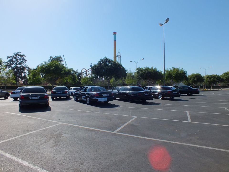Dark sedans angled in a parking lot with a tall striped drop tower behind trees