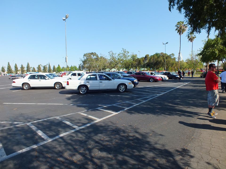 Man in red shirt stands near white sedans in a large open parking lot