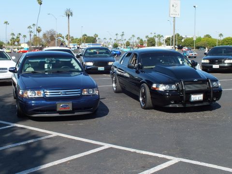Dark blue Ford sedan beside a blacked-out sedan with push bar in a lot