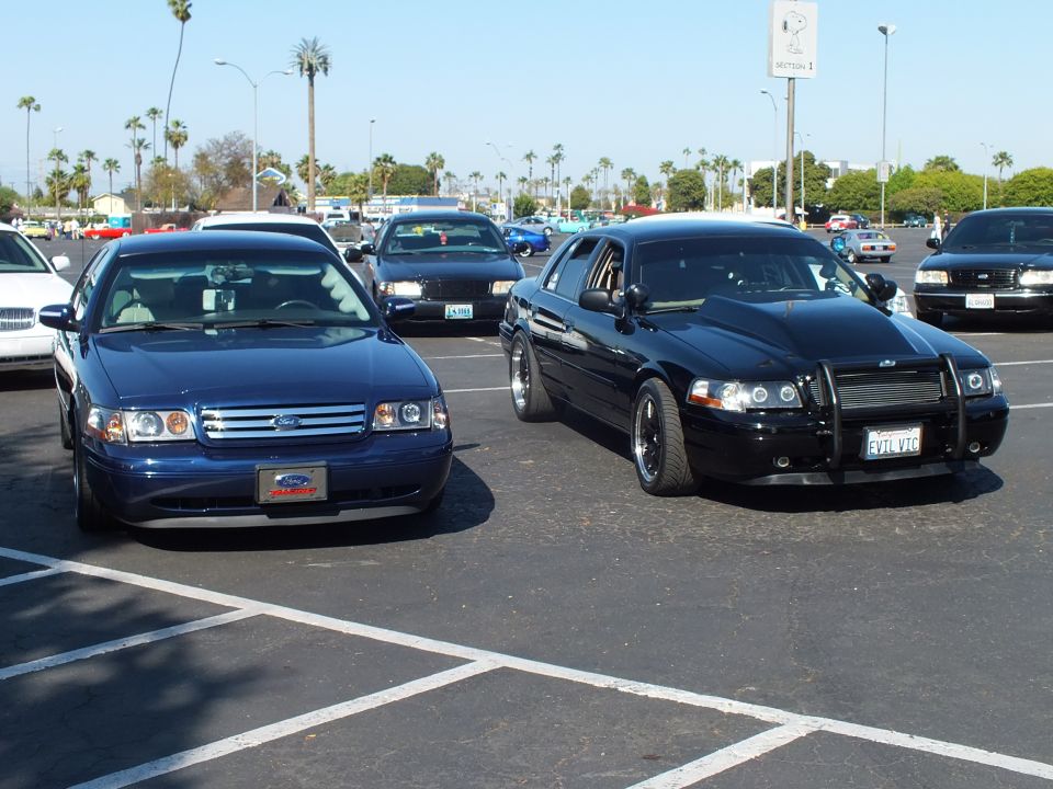 Dark blue Ford sedan beside a blacked-out sedan with push bar in a lot