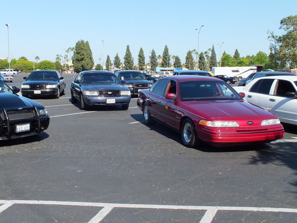 Maroon Ford full-size sedan parked among dark sedans in a sunny lot