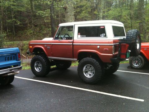 1992 Ford Bronco - Orange Ford Bronco, lifted, parked next to a blue Ford pickup truck.
