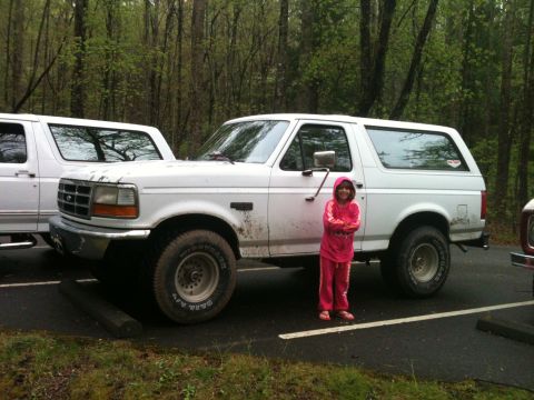 1992 Ford Bronco - A 1992 Ford Bronco is parked next to another vehicle, with a young girl standing by the driver's side door.