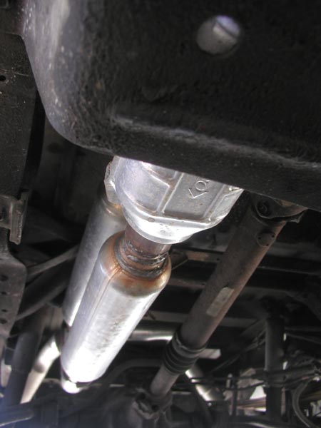 1988 Ford Bronco - Underbody view of a new aluminized catalytic converter and muffler inlet pipe running alongside the fuel tank, with heat discoloration at t…